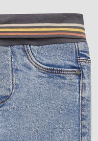 Denim jeans met een donkergrijze, gestreepte elastische tailleband. Kenmerken zijn onder andere twee voorzakken, contrasterende oranje stiksels en een gladde textuur.