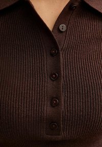Brązowa polo z prążkowanej dzianiny z kołnierzykiem i czterema ciemnymi guzikami, charakteryzująca się teksturowanym materiałem oraz pionowymi wzorami prążków.