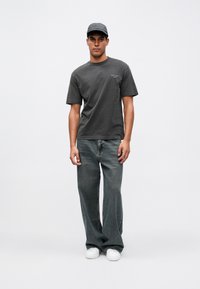 Camiseta de algodón gris oscuro con mangas cortas y un escote redondo, combinada con unos vaqueros de mezclilla desgastados de pierna ancha y zapatillas blancas.