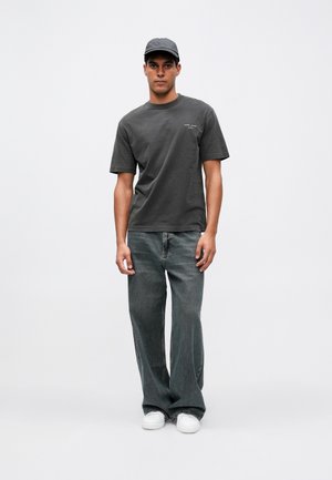 Tmavě šedé bavlněné tričko s krátkými rukávy a kulatým výstřihem, v kombinaci s širokými, vybledlými džínami a bílými teniskami.