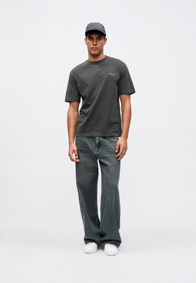 Camiseta de algodón gris oscuro con mangas cortas y un escote redondo, combinada con unos vaqueros de mezclilla desgastados de pierna ancha y zapatillas blancas.