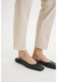 Zapatos de cuero negro tipo mocasín con punta cuadrada, combinados con pantalones ajustados de color beige claro que cuentan con aberturas laterales en el dobladillo.