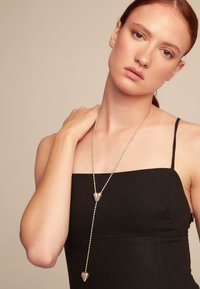 Collar de cuentas de plata con dos colgantes en forma de corazón, colgando entre el escote y el hombro de la persona que lo lleva, sobre un vestido negro.