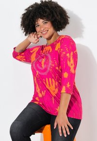 Helle pinke und orange Batik-langärmlige Bluse mit einem Smiley-Muster aus Strasssteinen. Kombiniert mit strukturierten schwarzen Hosen.
