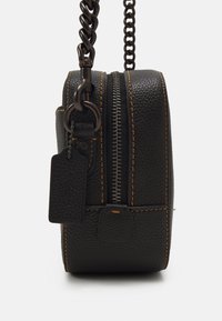 Černá kožená taška s texturovaným povrchem, oranžovým prošíváním, zaobleným tvarem, stříbrným zipem, řetízkovým popruhem a malou visačkou.