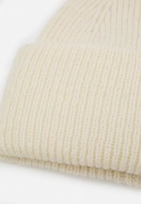 Knit beanie in cream color with ribbed texture. Features a folded cuff for a snug fit, made from soft, warm fabric.