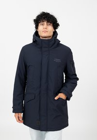 Marineblauer wasserdichter Parka mit hohem Kragen, Reißverschluss-Taschen und einem Logo auf der Brust. Verfügt über eine verstellbare Kapuze und elastische Bündchen.