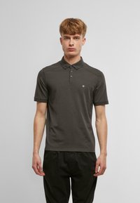 Tmavohnedá polo košeľa s gombíkovým golierom, krátkymi rukávmi a malým logom na hrudi. Mäkky, hladký materiál s úzkym strihom.