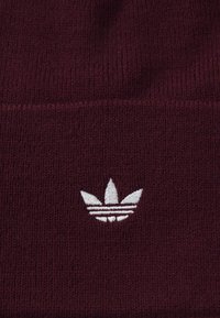 Cappello di lana di colore marsala con un logo a tre righe ricamato bianco sulla parte anteriore. Texture morbida con un design aderente.