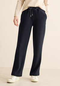 Pantalons amples de couleur marine en tissu texturé avec taille à cordon réglable, poches latérales, et associés à des baskets blanches.