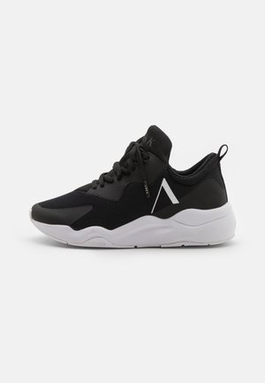 Czarny sportowy sneaker z białą podeszwą, siateczkową cholewką, sznurowaniem, uchwytem na pięcie i białym kanciastym logo z boku.