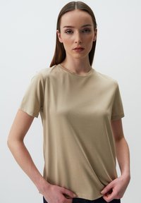 T-shirt beige a maniche corte realizzato in tessuto liscio, con scollatura rotonda e vestibilità rilassata, decorato con dettagli di cucitura minimalista.