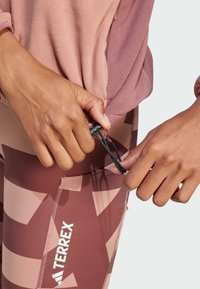 Urheiluvaatteet, joissa on vaaleanpunainen teksturoitu toppi ja kuvioidut ruskeat leggingsit. Leggingsit sisältävät taskun ja säädettävän nyörityksen.