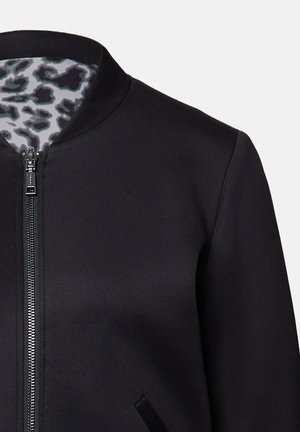 Schwarze Zip-Jacke mit Stehkragen, ausgestattet mit einem Innenfutter im Leopardenmuster und zwei seitlichen Taschen. Glattes, strukturiertes Gewebe.
