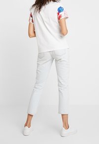 Biała koszulka z krótkimi rękawami w kwiatowy wzór, zestawiona z jasnoniebieskimi, skrojonymi dżinsami i białymi sneakersami. Prosty design, casualowy krój.