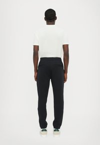 Black sweatpants with a smooth texture and two back pockets, paired with a plain white t-shirt and light-colored sneakers.