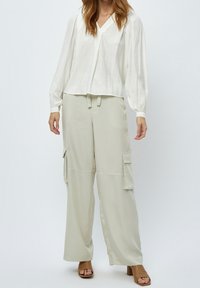 Lehká bílá blůza s dlouhým rukávem a výstřihem do V, doplněná volnými světlobežovými cargo kalhotami s bočními kapsami.