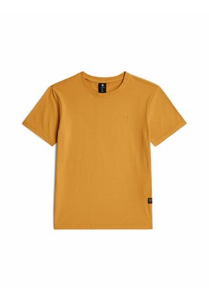 T-shirt en coton jaune moutarde à manches courtes avec encolure ronde et petite étiquette noire dans l'ourlet inférieur sur fond blanc.