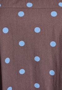 Brauner Stoff mit glatter Textur, der gleichmäßig verteilte hellblaue Punkte aufweist. Das Design ist einfach und geometrisch.