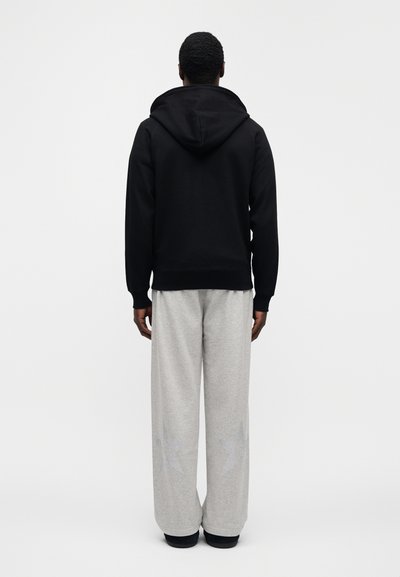 Μαύρο φούτερ με κουκούλα και ομαλή υφή, συνδυασμένο με ανοιχτό γκρι παντελό νι φόρμας με διακριτικά αστέρια. Και τα δύο έχουν άνετη εφαρμογή.