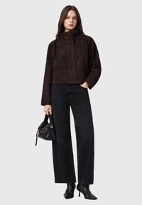 Giacca corta in camoscio marrone con collo alto, abbinata a jeans neri a gamba larga e stivali neri con tacco. Accessorio: piccola borsa nera.