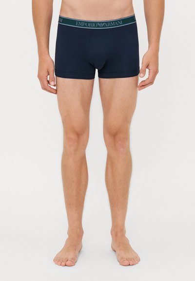 Marineblaue Boxershorts aus weicher Baumwolle mit einem elastischen Bund, der eine grüne Akzentuierung aufweist. Taillierte Passform, Oberschenkel-lange.