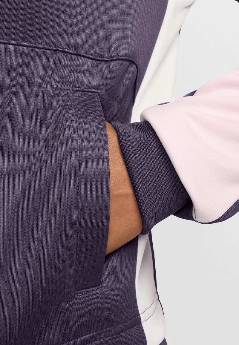 Sudadera púrpura con bolsillo tipo canguro, mangas en contraste rosa, tejido texturizado y puños acanalados para un detalle y estructura adicionales.