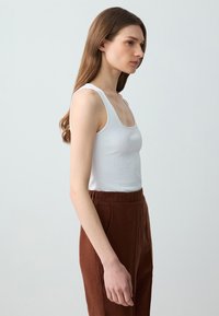 Weißes geripptes Tanktop mit breiten Trägern und einem runden Ausschnitt, kombiniert mit hoch taillierten braunen Leinenhosen mit elastischem Bund.
