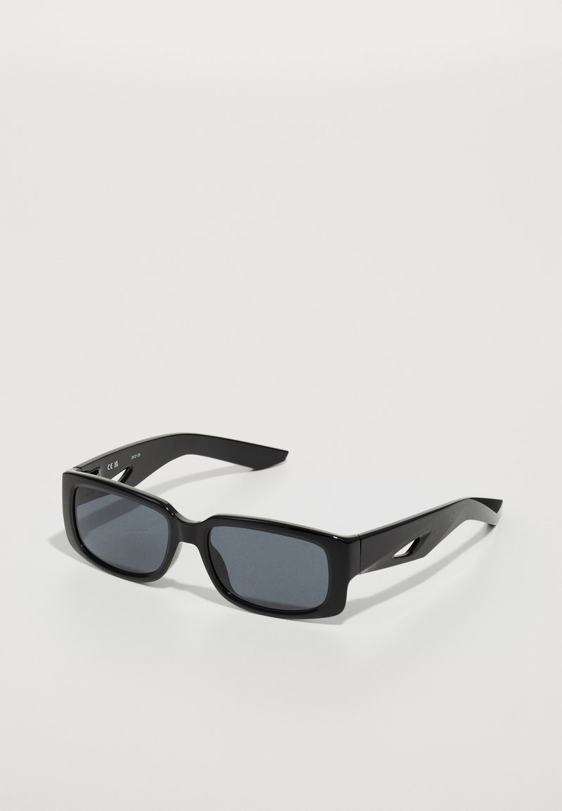Óculos de sol pretos com uma armação retangular, lentes escuras, textura suave e hastes anguladas com um detalhe recortado.