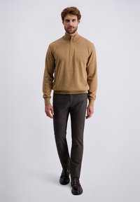 Pull en tricot beige avec un col zippé, associé à un pantalon gris foncé. L'ensemble présente une coupe ajustée et un tissu texturé.
