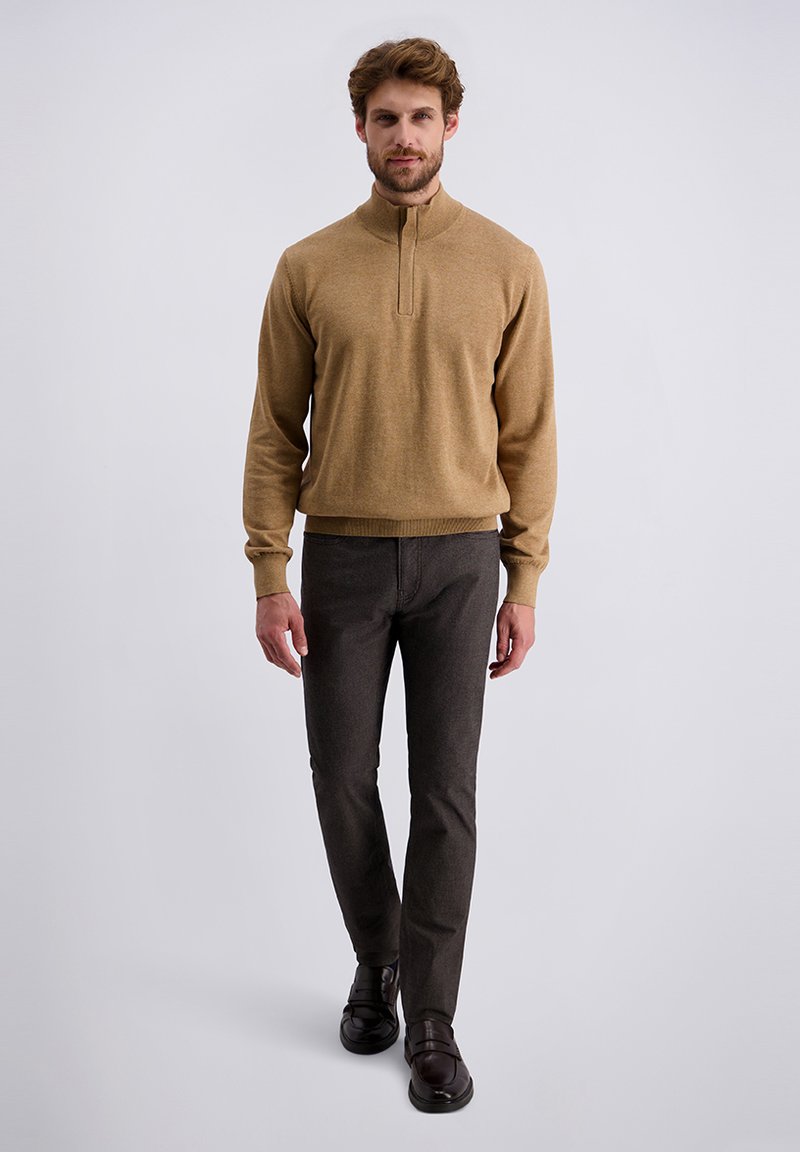 Pull en tricot beige avec un col zippé, associé à un pantalon gris foncé. L'ensemble présente une coupe ajustée et un tissu texturé.