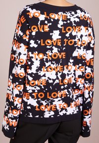 Sweat-shirt en polaire noir et blanc avec des lettres orange "LOVE TO", présentant une coupe décontractée, des manches longues, un tissu texturé et un large col.