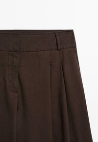 Bruine geplooide broeken met een gestructureerde stof, een vlakke tailleband en een zijzak, die een getailleerde pasvorm en strakke lijnen tonen.