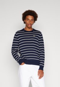 Marineblauwe gestreepte sweater van katoen, met witte horizontale strepen, geribbelde manchetten en een klein groen logo op de borst.