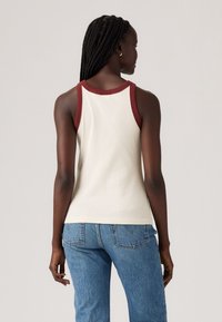Hvit ribbet tanktop med en maroon hals, tettsittende design og en enkel bak. Kombinert med lyseblå høyt liv-jeans.