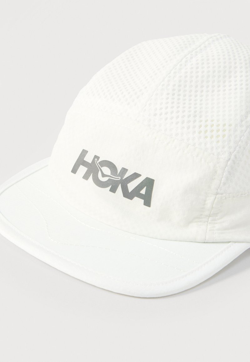 White breathable mesh running cap with curved brim and reflective "HOKA" logo on front panel.