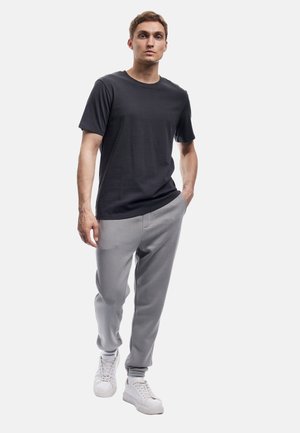 Herenoutfit bestaande uit een donkersgrijs katoenen t-shirt, lichtgrijze joggingsbroek met elastische boorden, en witte sneakers. Minimalistisch design en comfortabele pasvorm.