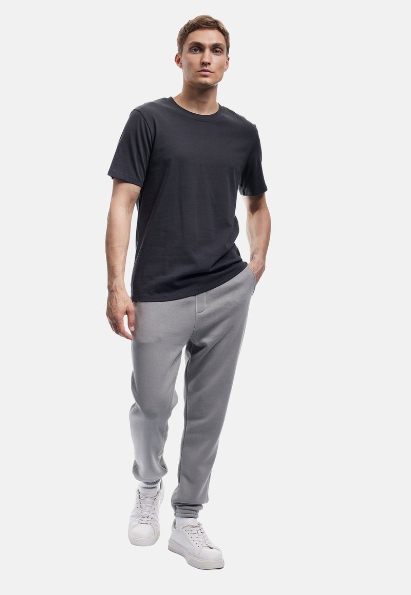 Herenoutfit bestaande uit een donkersgrijs katoenen t-shirt, lichtgrijze joggingsbroek met elastische boorden, en witte sneakers. Minimalistisch design en comfortabele pasvorm.