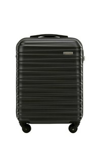 Valise rigide noire avec une texture de surface nervurée, une poignée robuste et quatre roues pour une mobilité aisée. Présente une plaque de logo sur le devant.
