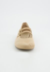 Chaussure Mary Jane en daim beige avec un bout arrondi, deux brides ajustables avec des boucles dorées, et une semelle intérieure rembourrée. Texture lisse, semelle plate.