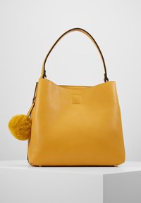 Bolso de cuero amarillo con forma estructurada, que cuenta con un acento de pompón suave y esponjoso. El interior es sencillo, maximizando el espacio.