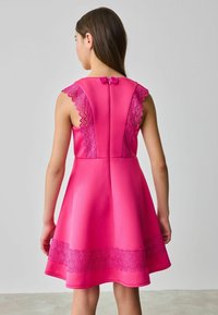 Fuchsia Kleid mit schwingendem Rock, Spitzenakzenten an den Schultern und einer Schleifendetails im Rücken. Glatte Textur und strukturierter Entwurf.