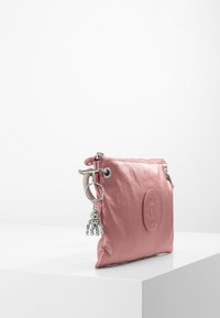 Rosa nylonpåse med dragkedja, med en cirkulär logotyp och en silver charm. Slät textur, liten storlek och minimalistisk design.