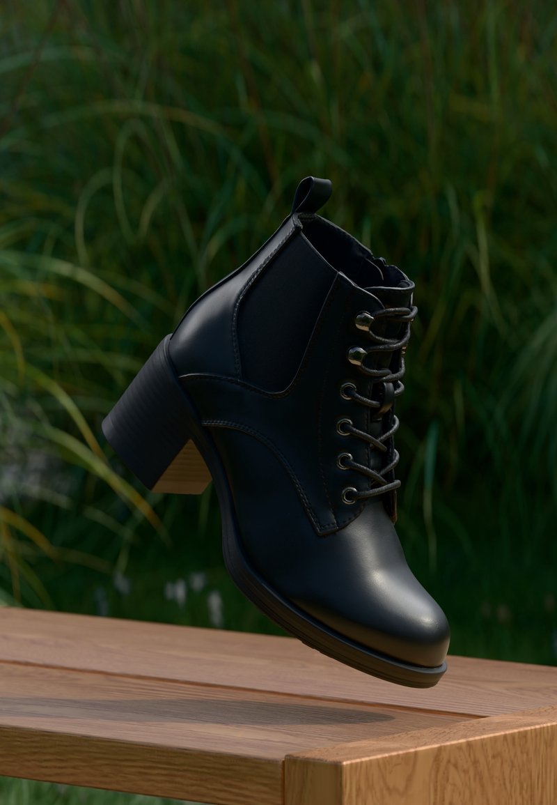 Bottine montante en cuir noir à lacets avec talon carré suspendue au-dessus d'une surface en bois, avec un feuillage vert flou en arrière-plan.