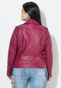 Aansluitende, bordeaux leren jack met epauletten en zilveren ritsen, met een soepele textuur en gestructureerde naden, gecombineerd met lichte jeans.