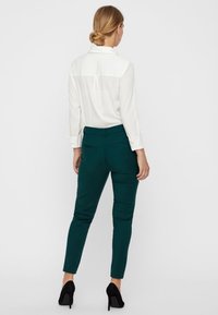 Biała bluzka z kołnierzykiem i karczkiem z tyłu, połączona z dopasowanymi, turkusowymi spodniami do kostek. Uzupełniona czarnymi, wysokimi szpilkami.