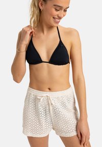 Czarny trójkątny biustonosz bikini z falbankami i białe, dziane szorty z wiązaniem oraz ażurowym wzorem.