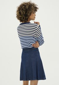 Prúžkovaný pletený sveter v modrej, krémovej a námorníckej farbe, skombinovaný s tmavomodrou áčkovou sukňou s záhybmi, ktorý ukazuje rebrovanú textúru a ležérny štýl.