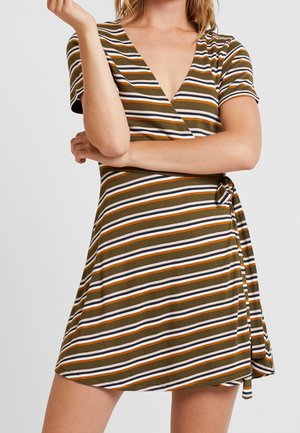 Femme portant une robe portefeuille à manches courtes et col en V avec des rayures horizontales marron, orange, blanc et noir, bras croisés à la taille.
