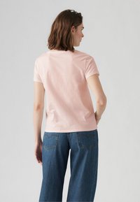 Ljusrosa t-shirt med rund halsringning och korta ärmar, i kombination med högmidjade blå denimjeans med bakfickor och sömnadsdetaljer.